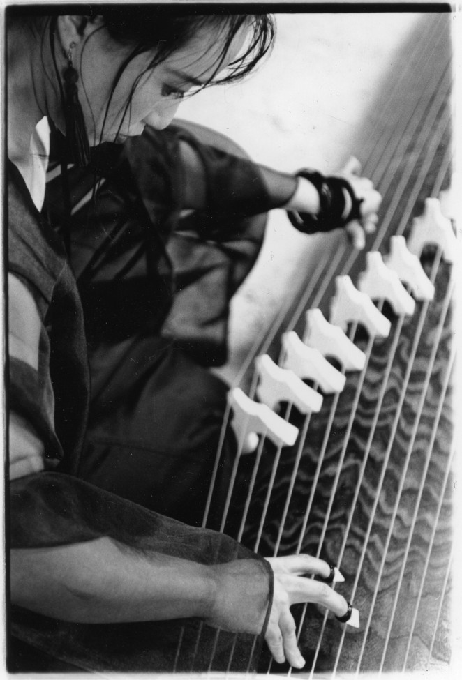Michiyo Yagi close portrait plucking and bending strings of her koto in black & white